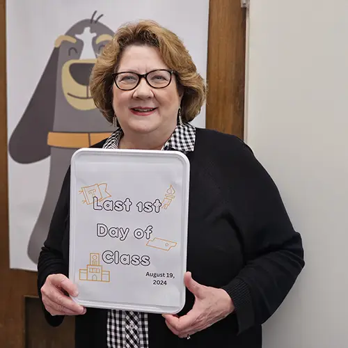 A woman holding a sign that says "Last First Day of Class"