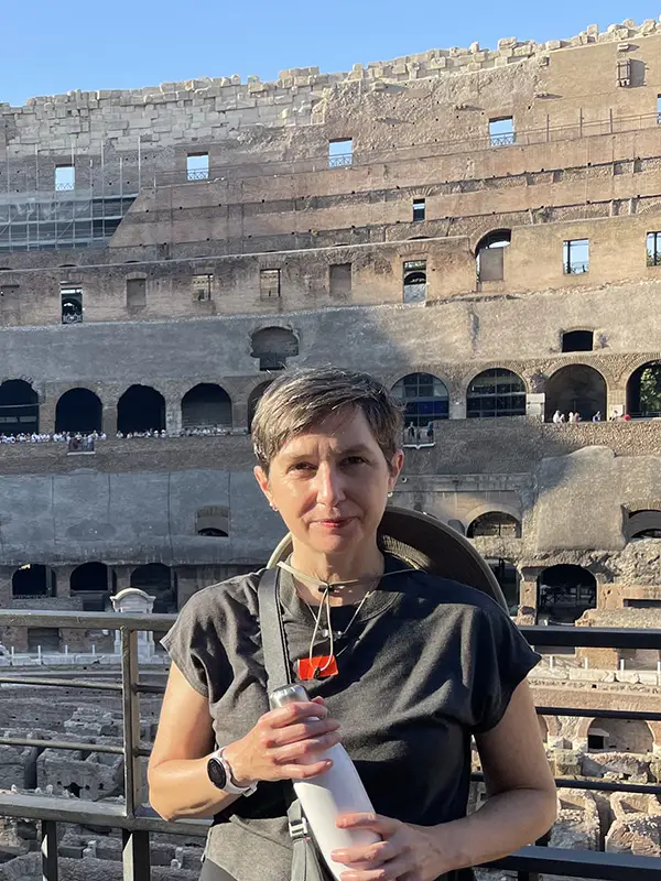 A woman with a water bottle takes a photo with the coliseum behind her